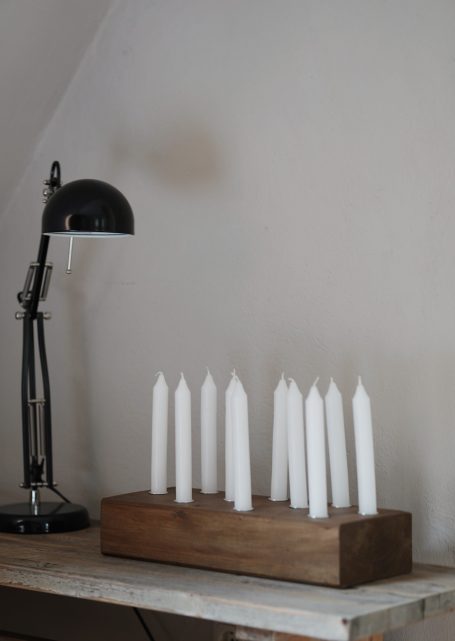 Ein Kerzenhalter aus Massivholz mit mehreren weißen Kerzen und einer schwarzen Schreibtischlampe daneben.
