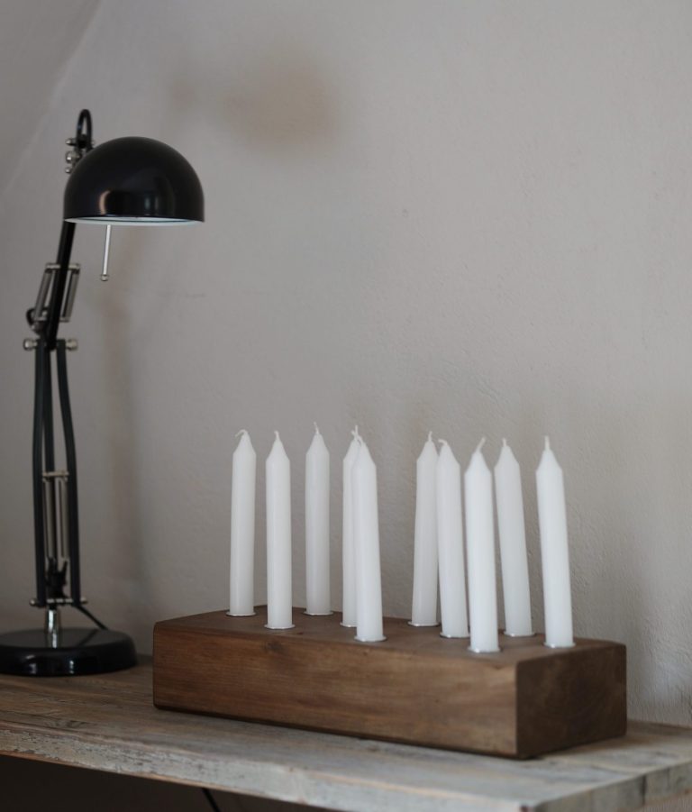 Eine moderne Tischlampe neben einem Kerzenständer mit weißen Kerzen auf Holz