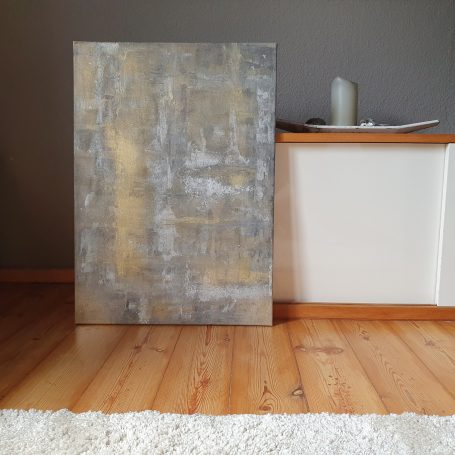 Grau, goldenes Wandbild vor einem weißen Sideboard und auf einem hellen Holzboden.