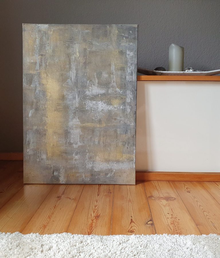 Abstraktes Wandbild in Grautönen mit goldenen Akzenten, auf einem hellen Holzboden.