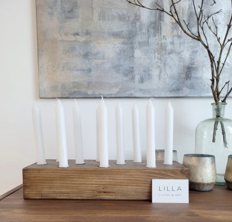 Zehn weiße Kerzen in einem Holzkerzenständer, daneben eine Visitenkarte mit dem Namen "LILLA Living & Art".