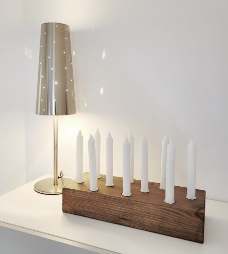 Moderne Tischlampe neben einem Kerzenhalter mit weißen Kerzen auf einem Holzsockel.