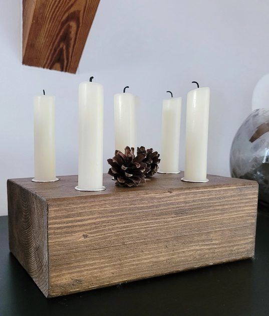 Kerzenblock aus Holz mit fünf weißen Kerzen und einem Tannenzapfen als Dekoration.